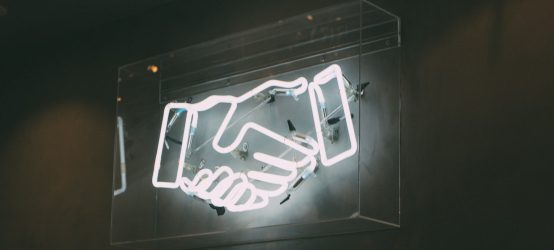 Neon Sign Depicting a Handshake (via Unsplash.com)